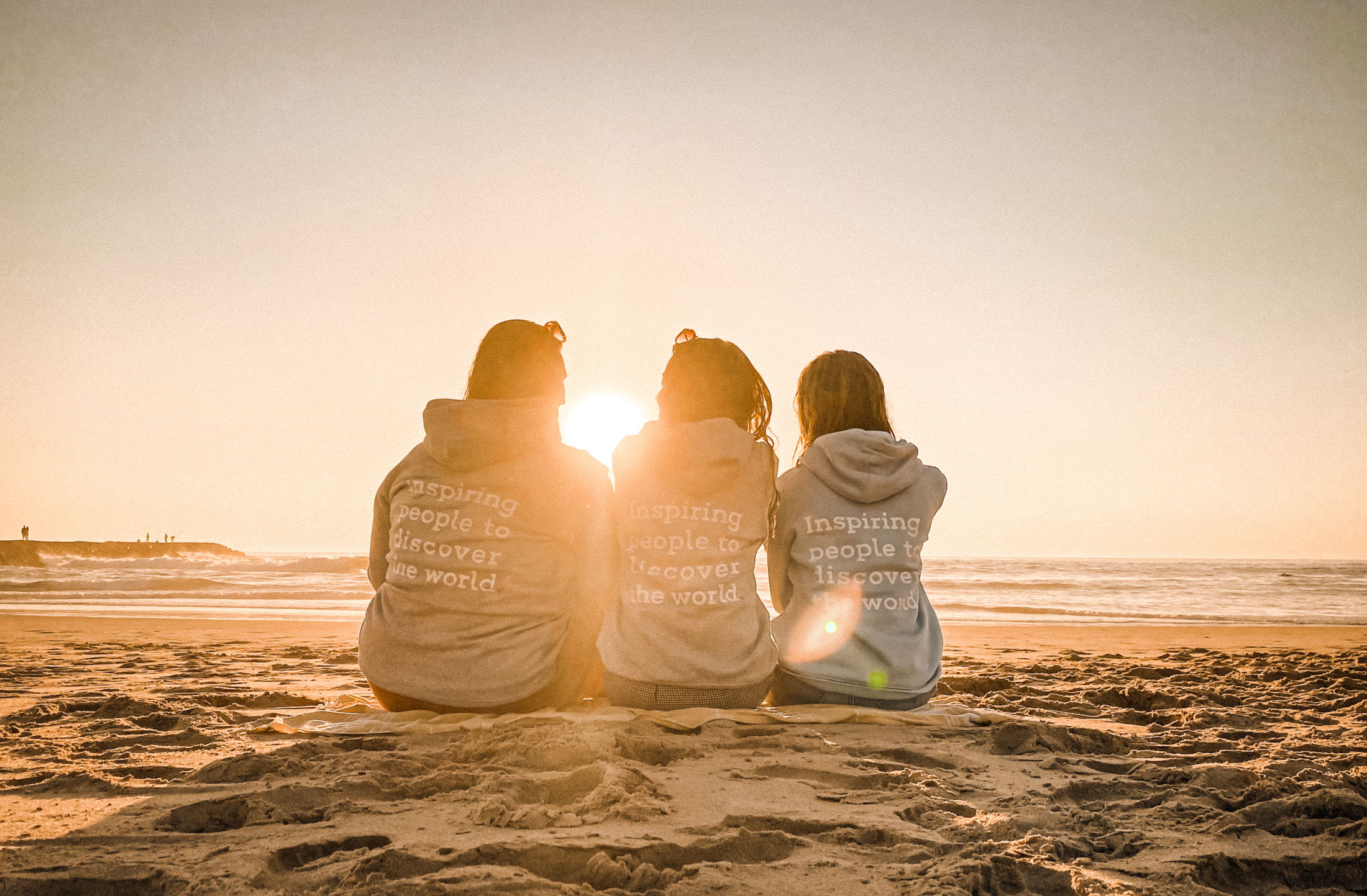 Gruppe von Freunden, die am Strand spazieren. Der Mann in der Mitte trägt eine Frau auf dem Rücken.