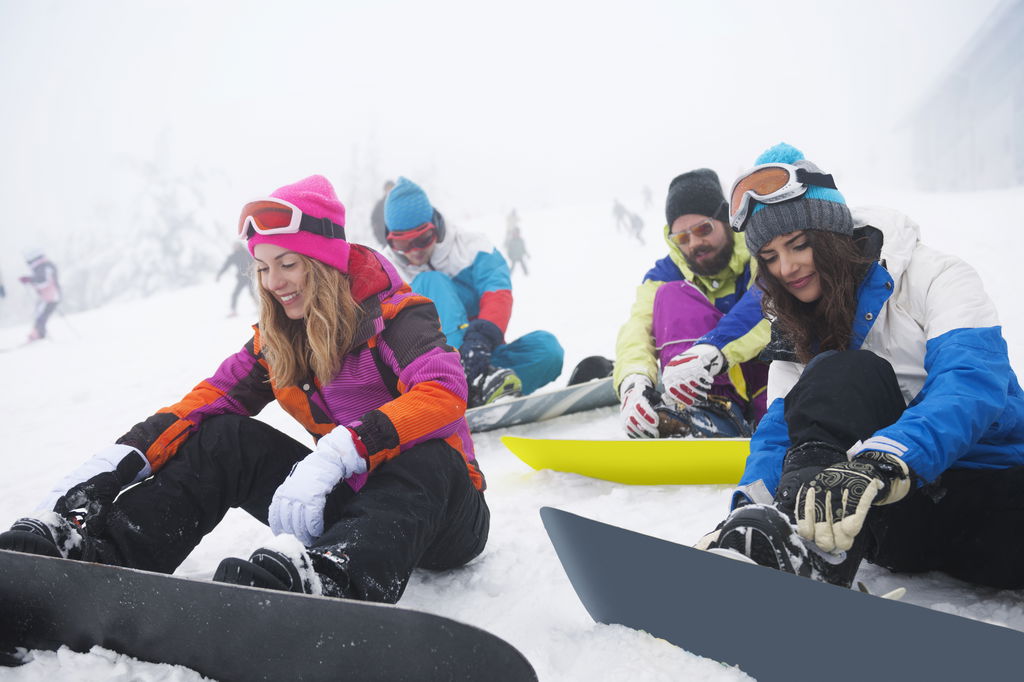 Group of friends sitting in the snow with snowboards